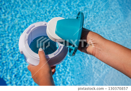 Hands placing chlorine tablet into pool dispenser for water treatment and maintenance 130370857