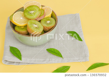 Fruits in a plate. Kiwi and lemon sliced in a green plate on a yellow background. Fruits in a plate. Kiwi and lemon sliced in a green plate on a yellow background. 130370932