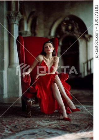 A woman in a red dress sits in a red chair 130371183