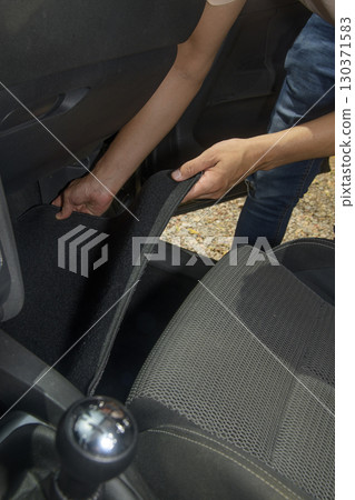 man installing a new black carpet mat inside a car 130371583