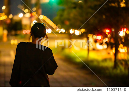 A woman walking alone on the sidewalk at night 130371848