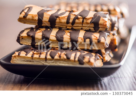 Sfogliatine glassate with chocolate. Italian crispy dessert on plate on wooden table. 130373045