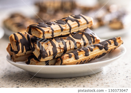 Sfogliatine glassate with chocolate. Italian crispy dessert on plate on kitchen table. 130373047