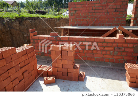 Skilled workers are constructing a brick wall with red bricks at a construction site. 130373066