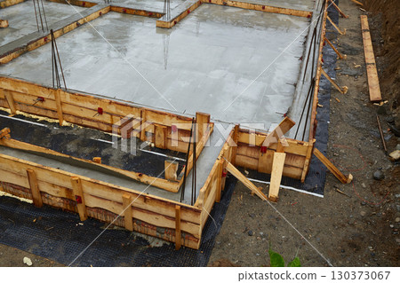 Construction of a concrete foundation with wooden forms at a building site on a cloudy day Construction of a concrete foundation with wooden forms at a building site on a cloudy day 130373067