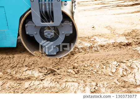Construction site features a blue roller compacting earth on a freshly excavated ground during daylight hours Construction site features a blue roller compacting earth on a freshly excavated ground during daylight hours 130373077