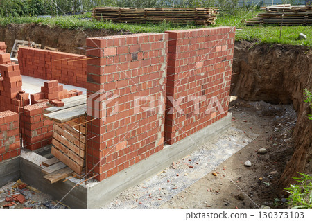 Brick wall construction in progress at a building site during daylight hours Brick wall construction in progress at a building site during daylight hours 130373103