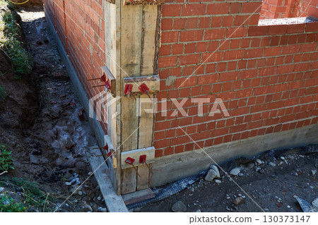 Brick walls are rising at a construction site, supported by wooden forms and metal rods. 130373147