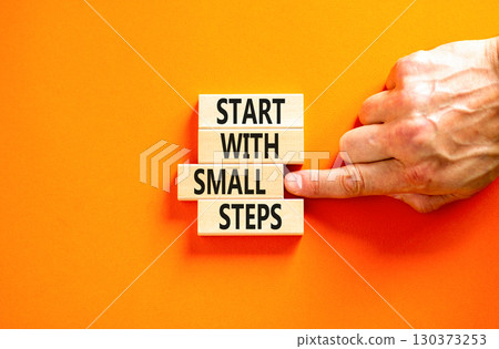 Start with small steps symbol. Concept words phrase Start with small steps on beautiful wooden blocks. Beautiful orange background. Businessman hand Business Start with small steps concept. Copy space Start with small steps symbol. Concept words phrase Start with small steps on beautiful wooden blocks. Beautiful orange background. Businessman hand Business Start with small steps concept. Copy space 130373253