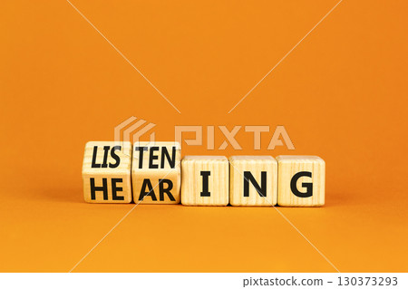 Listening or hearing symbol. Turned wooden cubes and changed a concept word Listening to Hearing. Beautiful orange background. Copy space. Business educational listening or hearing concept. 130373293