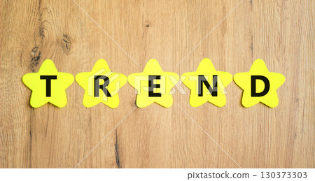 Trend and trending symbol. Concept word Trend on beautiful yellow paper stars. Beautiful wooden table wooden background. Business lifestyle trend and trending concept. Copy space. 130373303