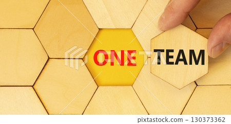 One team symbol. Concept word One team on beautiful wooden puzzles. Businessman's hand. Beautiful yellow paper background. Business one team concept. Copy space. One team symbol. Concept word One team on beautiful wooden puzzles. Businessman's hand. Beautiful yellow paper background. Business one team concept. Copy space. 130373362