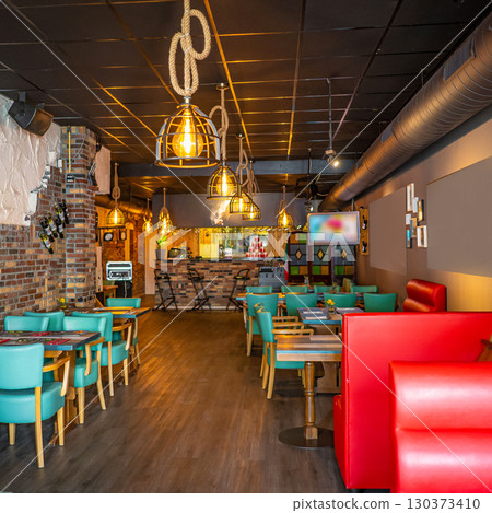 Half-lighted hall in a loft style restaurant open kitchen background. Half-lighted hall in a loft style restaurant open kitchen background. 130373410