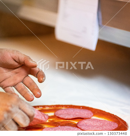 Hands preparing a pizza putting salami on pizza Hands preparing a pizza putting salami on pizza 130373448