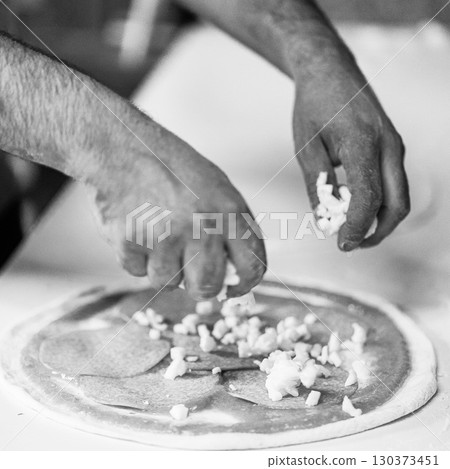 Hands preparing a pizza putting salami on pizza 130373451