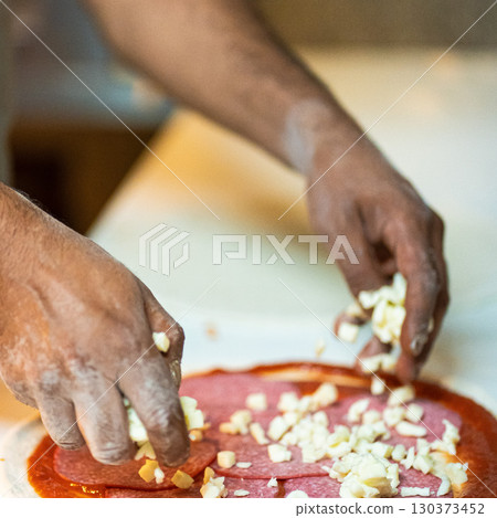 Hands preparing a pizza putting cheese mozzarella on pizza 130373452