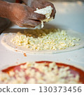 Hands preparing a pizza putting cheese mozzarella on pizza 130373456