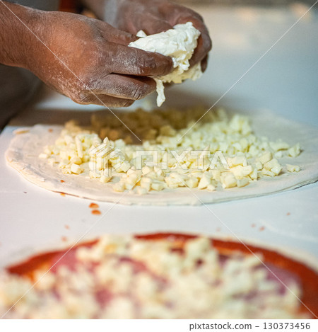 Hands preparing a pizza putting cheese mozzarella on pizza 130373456