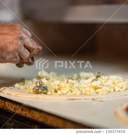Hands preparing a pizza putting cheese mozzarella on pizza Hands preparing a pizza putting cheese mozzarella on pizza 130373459