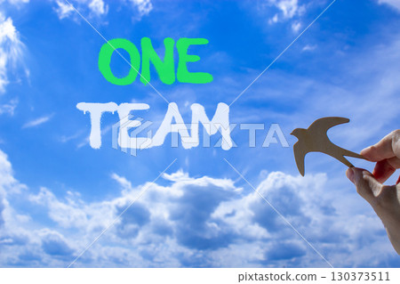 One team symbol. Concept word One team on beautiful blue sky. Businessman's hand with wooden bird. Beautiful blue sky and cloud background. Business one team concept. Copy space. 130373511