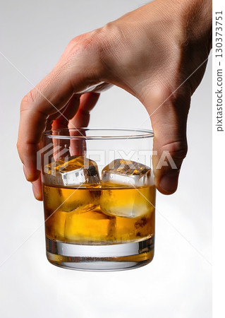 Hand holding glass of amber whiskey with ice cubes, condensation on the surface 130373751