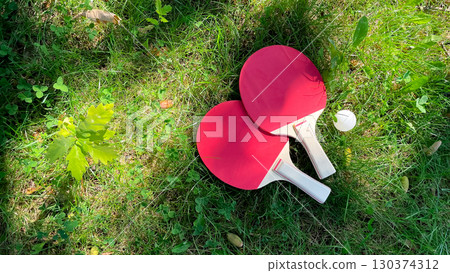 Table tennis rackets and balls on green grass, outdoor leisure 130374312