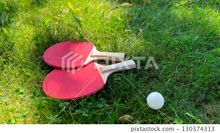 Table tennis rackets and balls on green grass, outdoor leisure 130374313