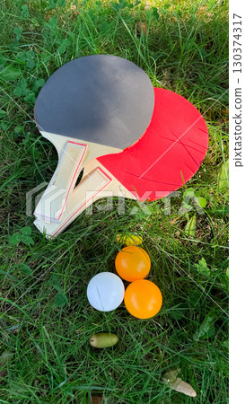 Table tennis rackets and balls on green grass, outdoor leisure 130374317