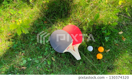 Table tennis rackets and balls on green grass, outdoor leisure 130374320