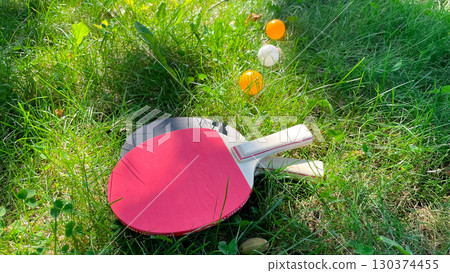 Table tennis rackets and balls on green grass, outdoor leisure 130374455
