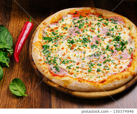 Freshly baked pizza topped with cheese, ham, and herbs on wooden table Freshly baked pizza topped with cheese, ham, and herbs on wooden table 130374946