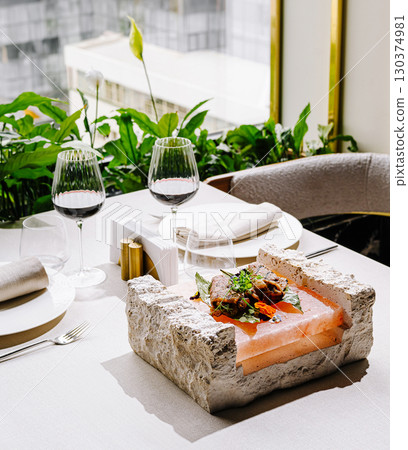 Elegant restaurant table setting with gourmet dish served on Himalayan salt block inside stone holder 130374981