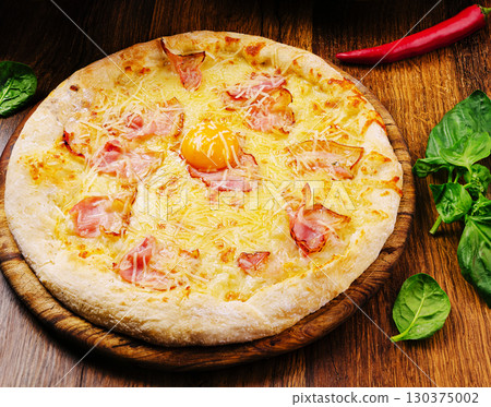 Delicious pizza topped with egg and ham served on a wooden board Delicious pizza topped with egg and ham served on a wooden board 130375002