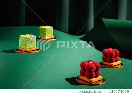 Exquisite dessert display with colorful cakes on green backdrop Exquisite dessert display with colorful cakes on green backdrop 130375009