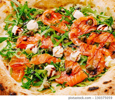 Delicious pizza topped with smoked salmon and fresh greens at a restaurant Delicious pizza topped with smoked salmon and fresh greens at a restaurant 130375059