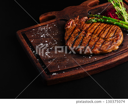 Grilled steak served on a wooden board with asparagus and sauce 130375074