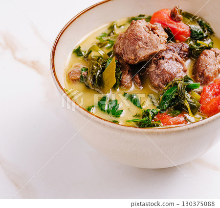 Delicious meat soup with greens served in a bowl during a cozy meal 130375088