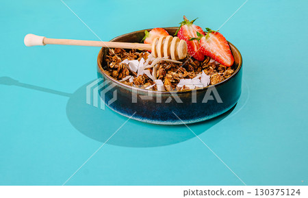 Healthy granola bowl with honey and strawberries on a turquoise background 130375124