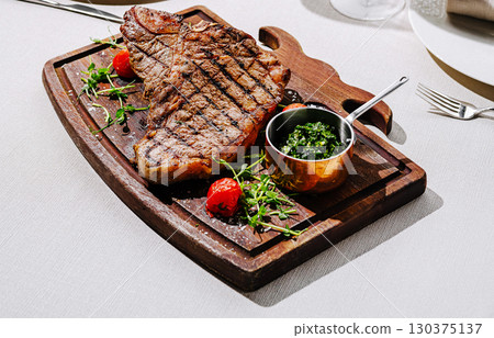 Large grilled steak served on a wooden board with herbs and sauce Large grilled steak served on a wooden board with herbs and sauce 130375137