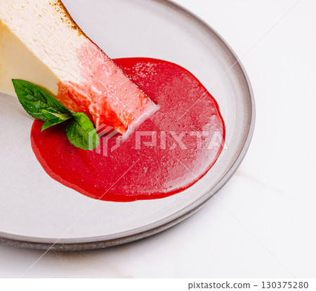 Delicious cheesecake slice with berry sauce and mint garnish on a plate Delicious cheesecake slice with berry sauce and mint garnish on a plate 130375280
