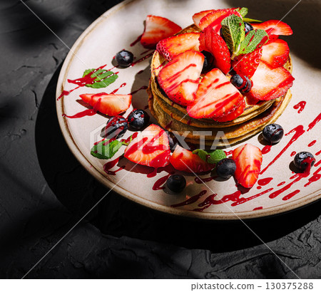 Fluffy pancakes topped with fresh strawberries and blueberries on a plate Fluffy pancakes topped with fresh strawberries and blueberries on a plate 130375288