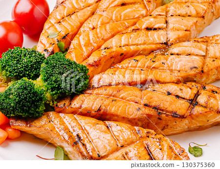 Grilled salmon fillets served with fresh vegetables on a white plate Grilled salmon fillets served with fresh vegetables on a white plate 130375360