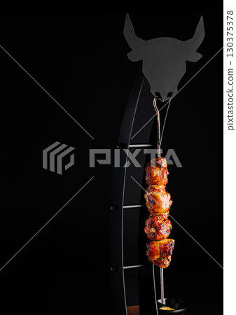 Delicious meat skewer hanging on artistic grill display in dark setting Delicious meat skewer hanging on artistic grill display in dark setting 130375378