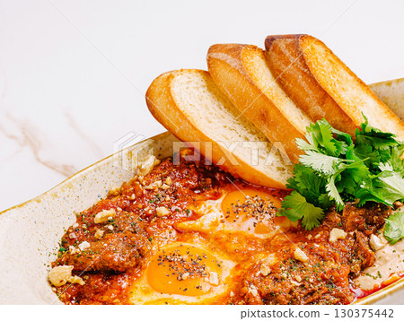 Delicious breakfast featuring baked eggs with sauce and toasted bread Delicious breakfast featuring baked eggs with sauce and toasted bread 130375442