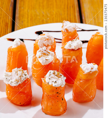 Delicious salmon rolls topped with creamy cheese on a wooden table 130375475