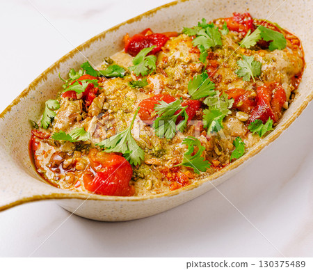 Delicious baked dish with peppers and herbs on a white table 130375489