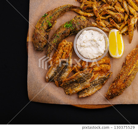Crispy fried fish and vegetables arranged on a wooden platter with sauce 130375529