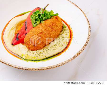 Deliciously plated meal featuring savory croquette and grilled pepper Deliciously plated meal featuring savory croquette and grilled pepper 130375536