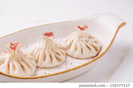 Delicious khinkali served on a stylish plate with a sprinkle of seasoning 130375537