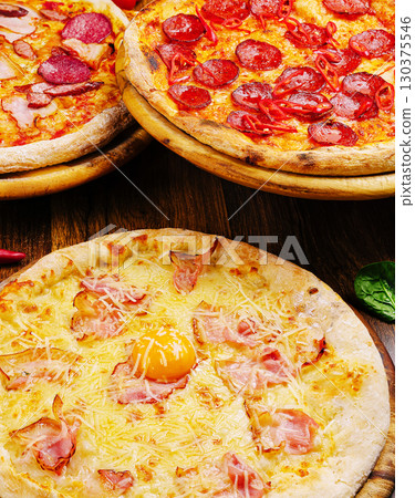 Delicious variety of pizzas served on wooden boards at a cozy restaurant Delicious variety of pizzas served on wooden boards at a cozy restaurant 130375546